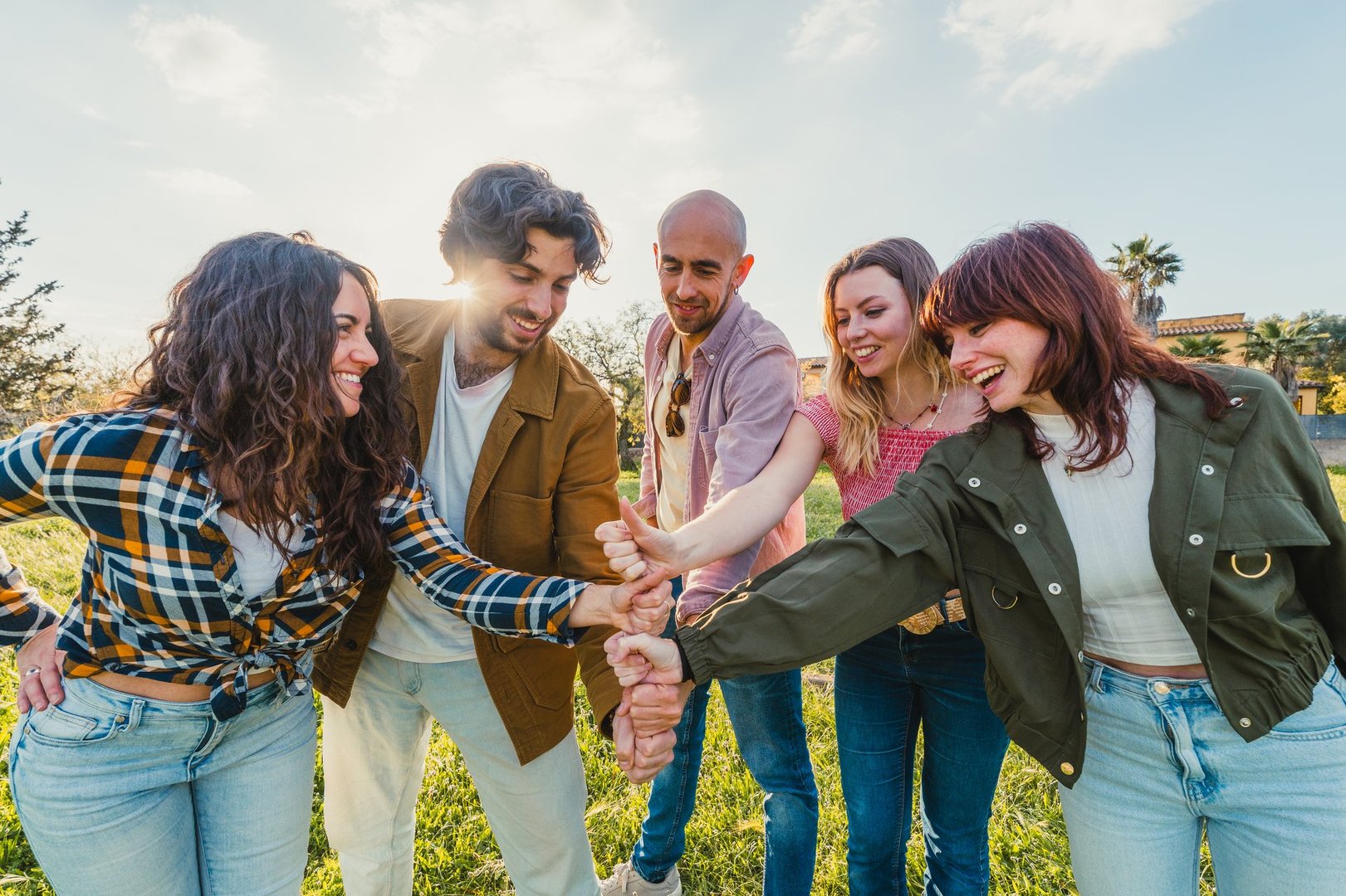 Young friends laughing while joining hands in a circle during an outdoor gathering - Friendship and Union Concept