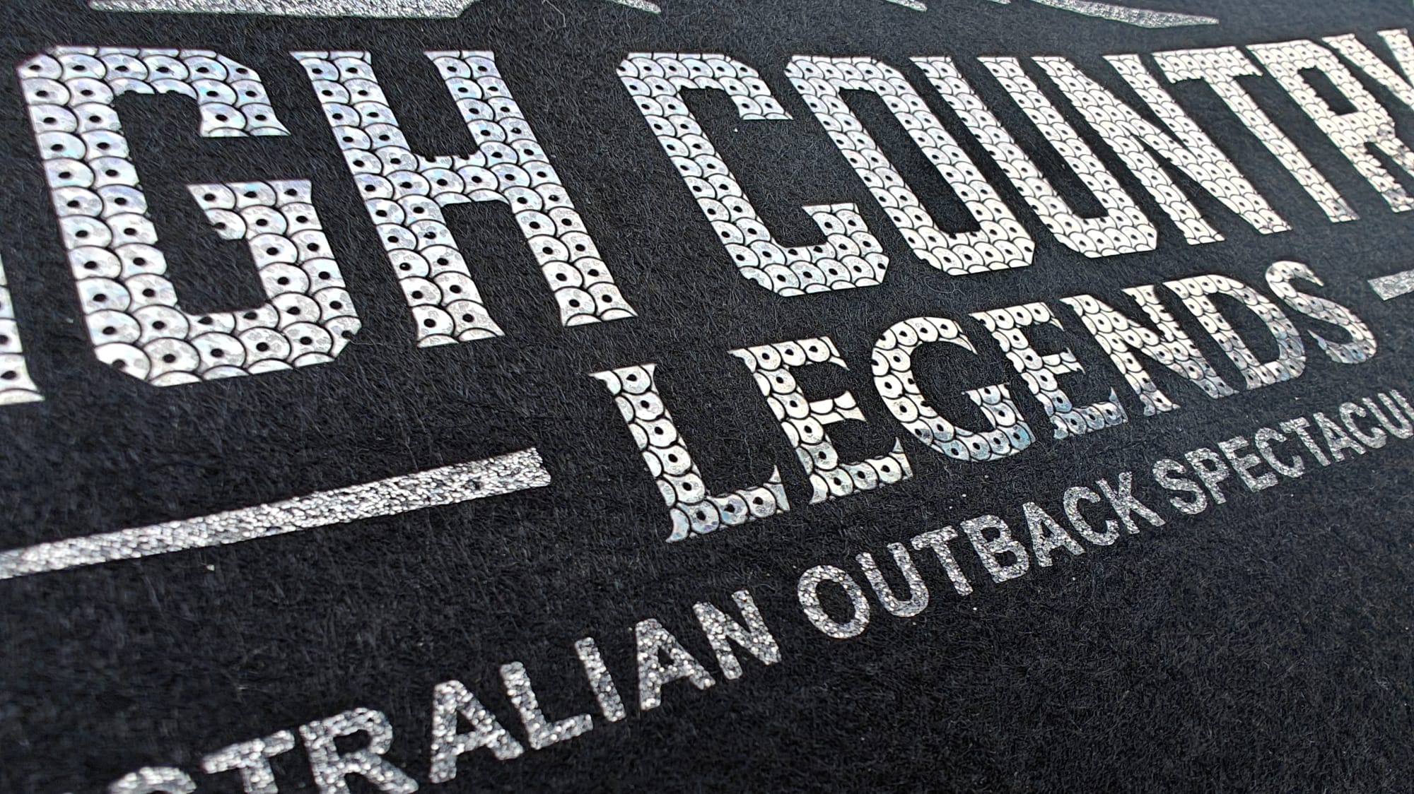 Close-up of textured lettering on fabric reading High Country Legends and Australian Outback Spectacular.