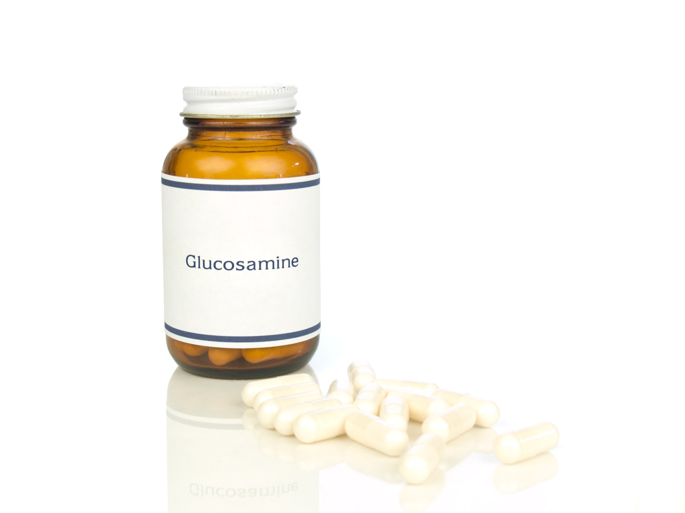 A brown bottle labeled Glucosamine with white capsules scattered in front on a white surface.