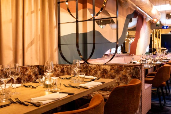 Elegant restaurant interior with stylish decor, tables set with glasses and napkins, and contemporary wall art.