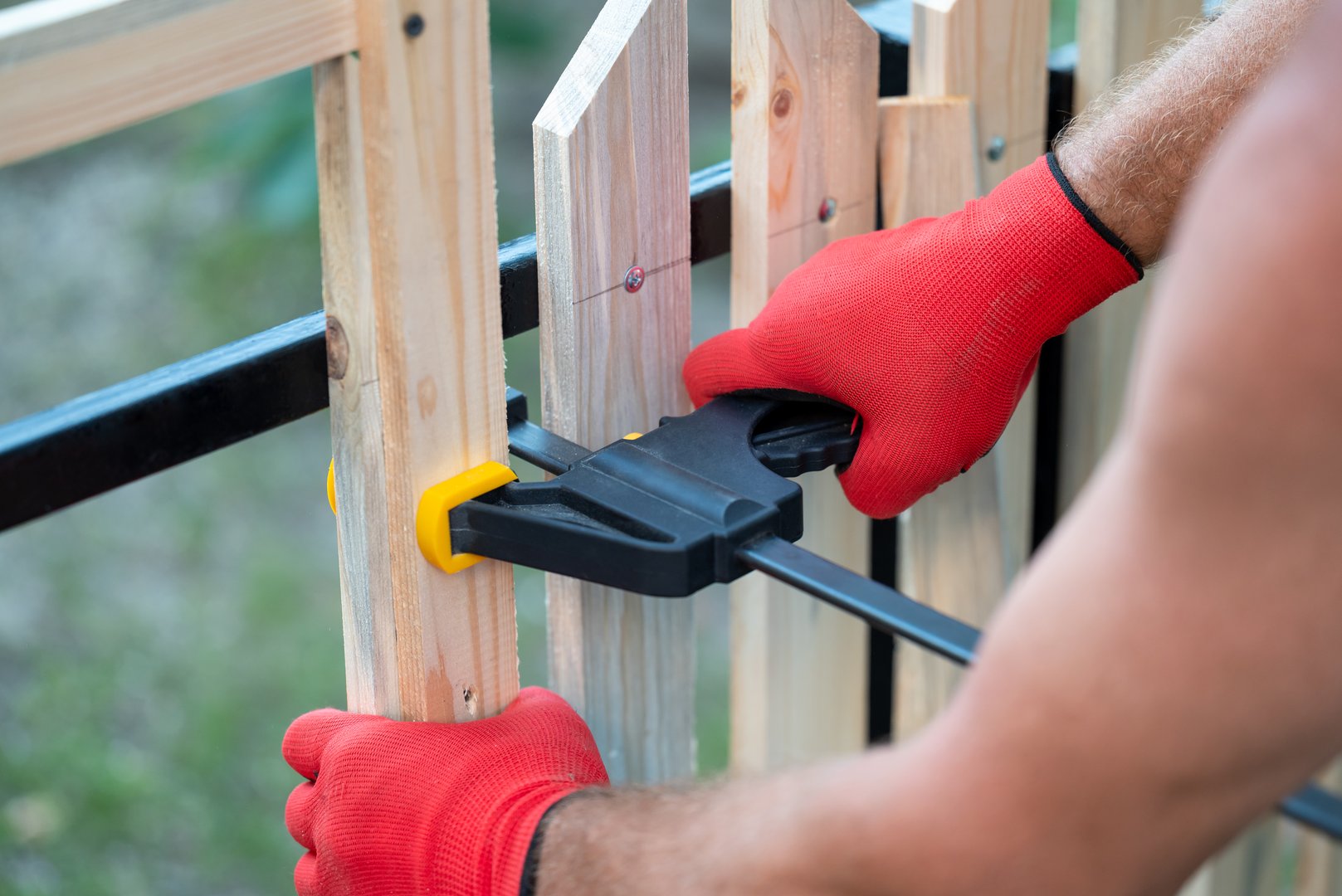 Hands of a man builder using bracket to attach planks to fence with same distance