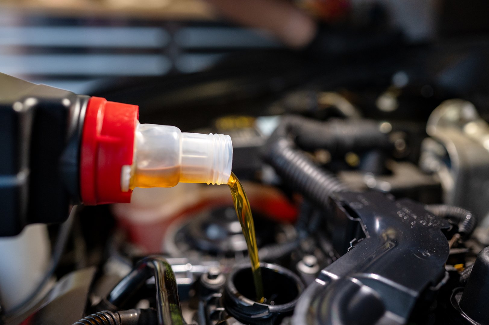 Close-up of engine oil being poured into a modern car engine during a maintenance procedure.