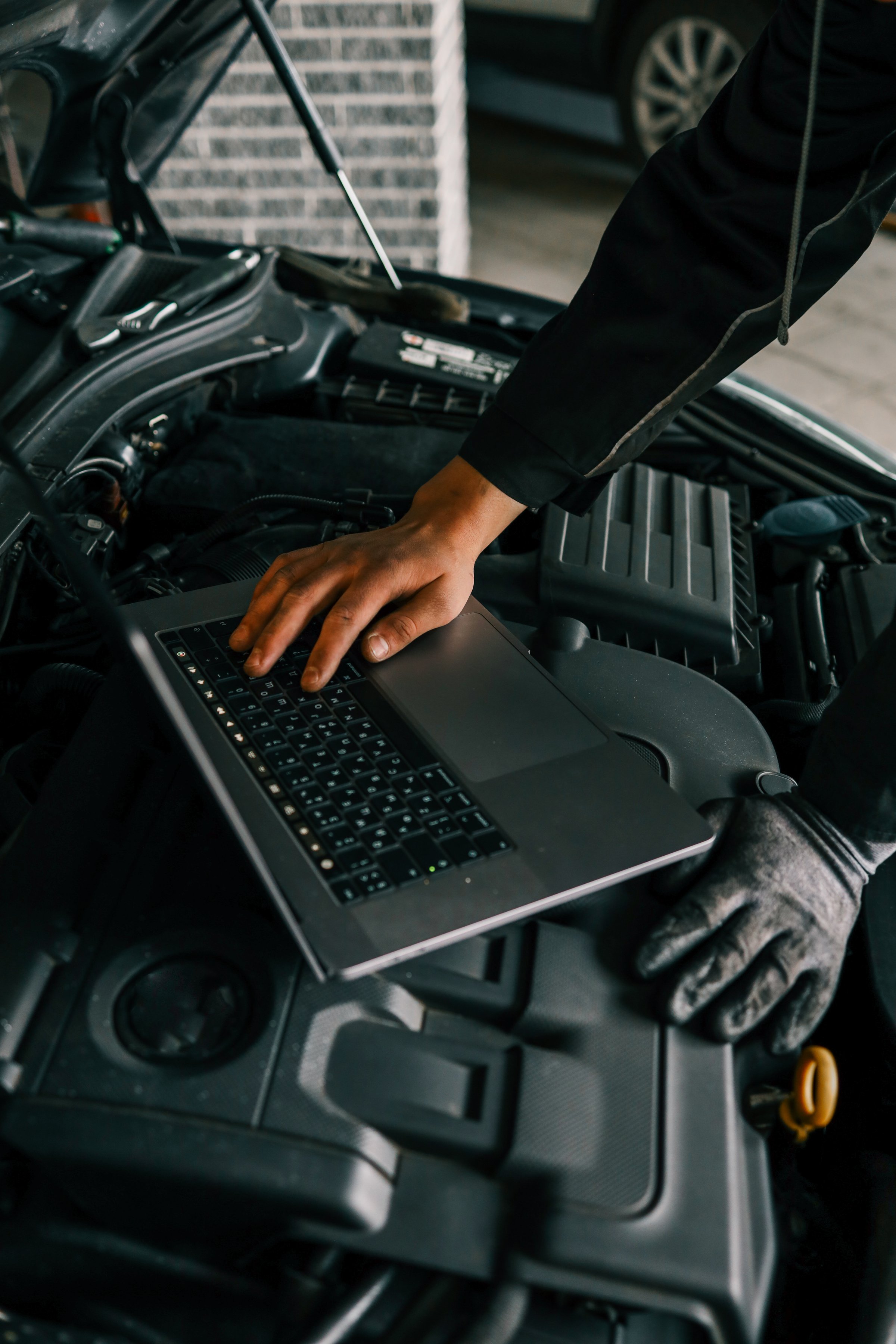 A mechanic using a laptop on a car engine for diagnostics in a garage. Highlights the use of technology in modern vehicle maintenance and repair.