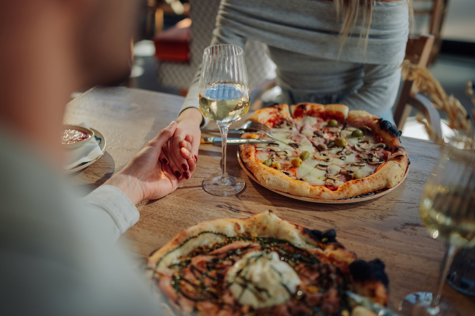 Romantic couple holding hands while enjoying pizza and wine at a restaurant table, celebrating their love and connection