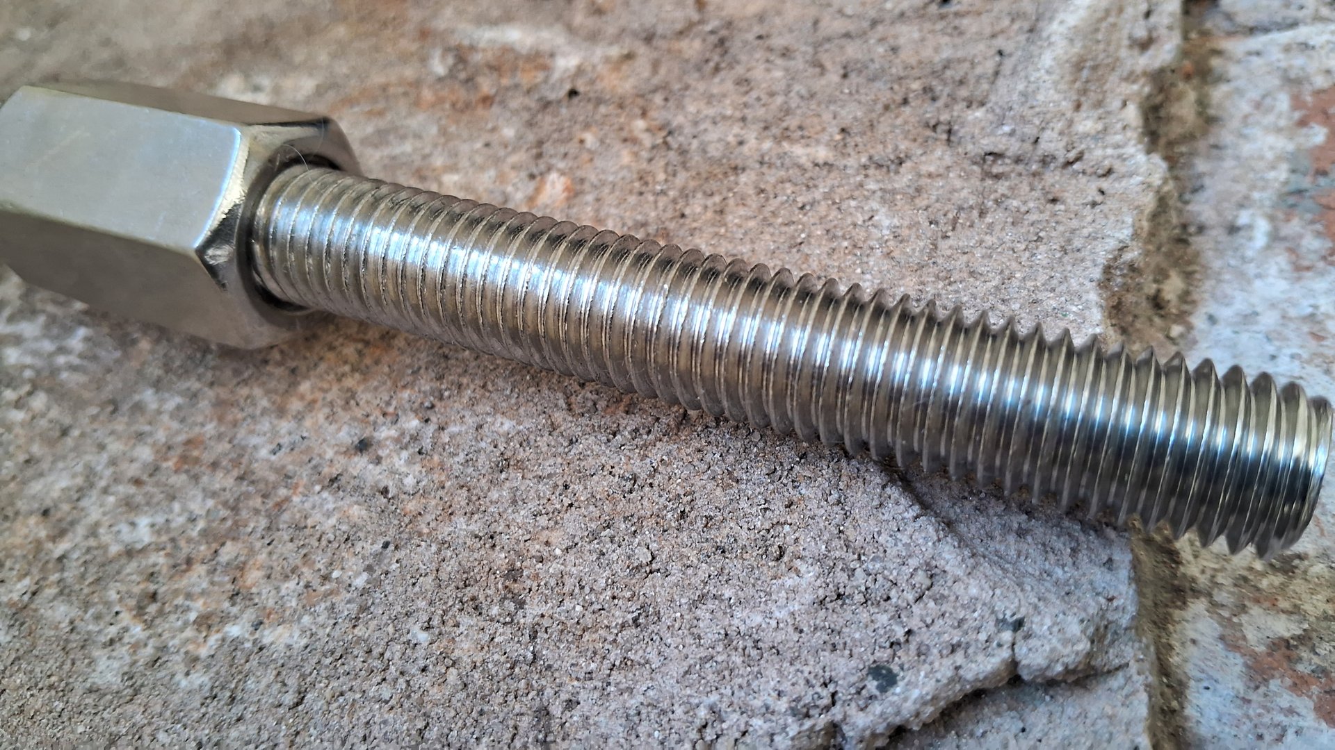 Close-up of a stainless steel threaded rod with a nut attached, highlighting the metallic finish and precise engineering details.