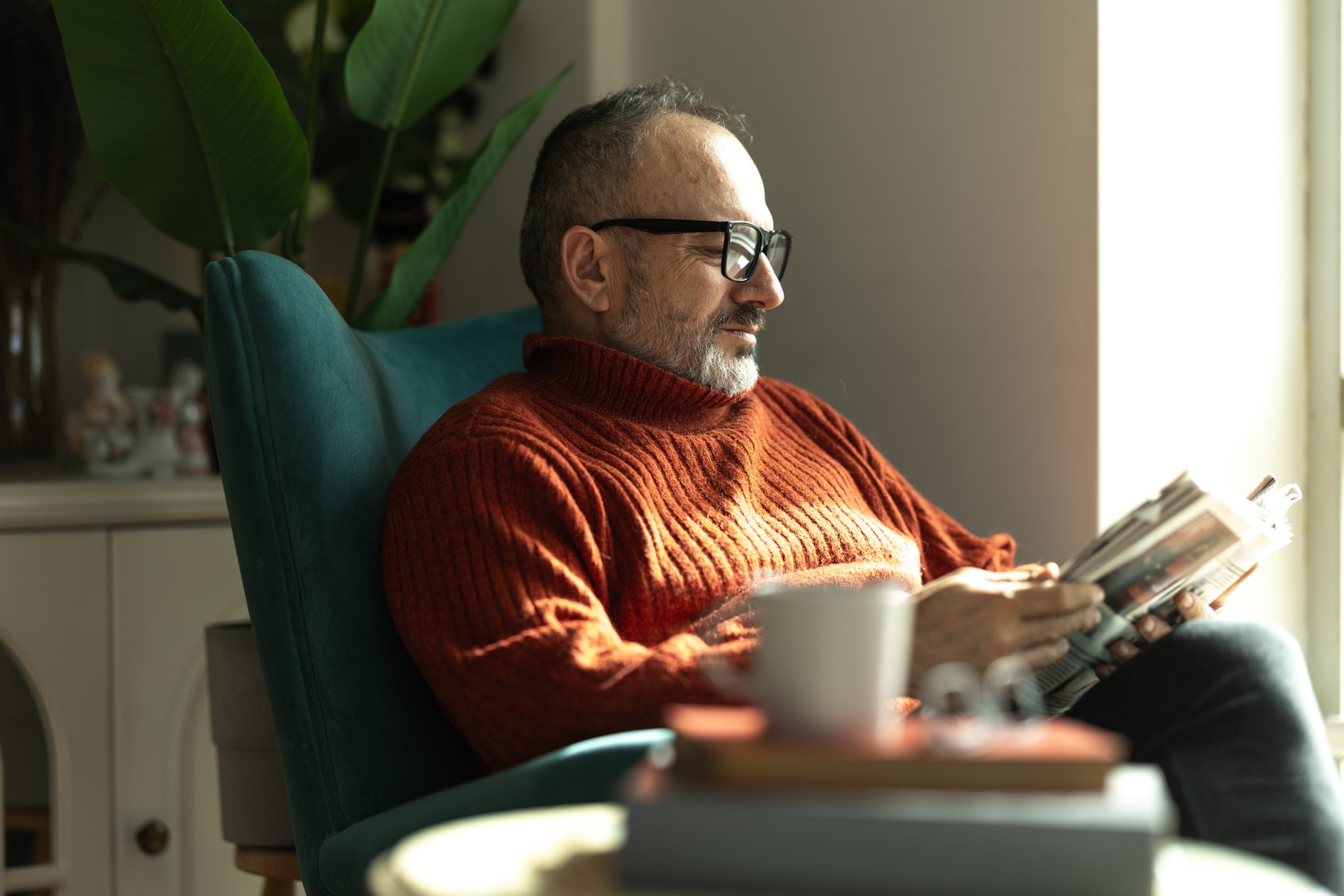 Mature man sitting in armchair, reading magazine and enjoying a quiet moment at home