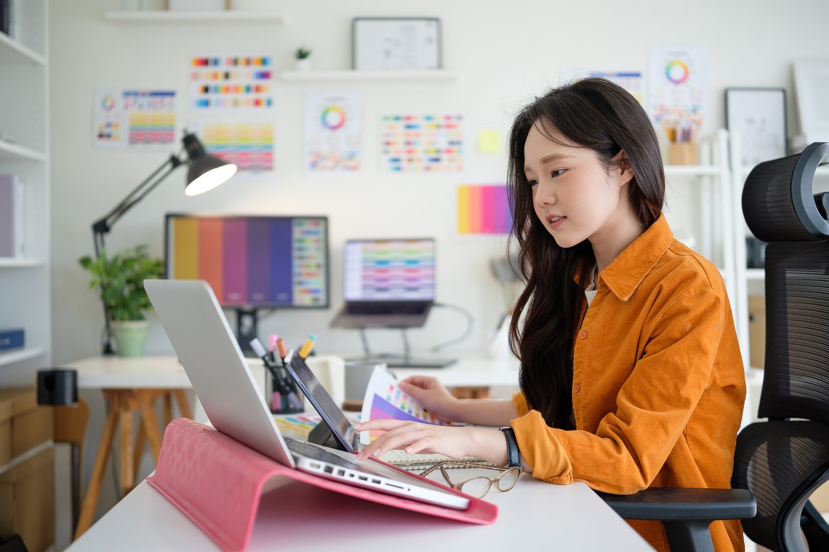 Young female designer concentrating on her project at a modern workspace with a laptop and color palettes.
