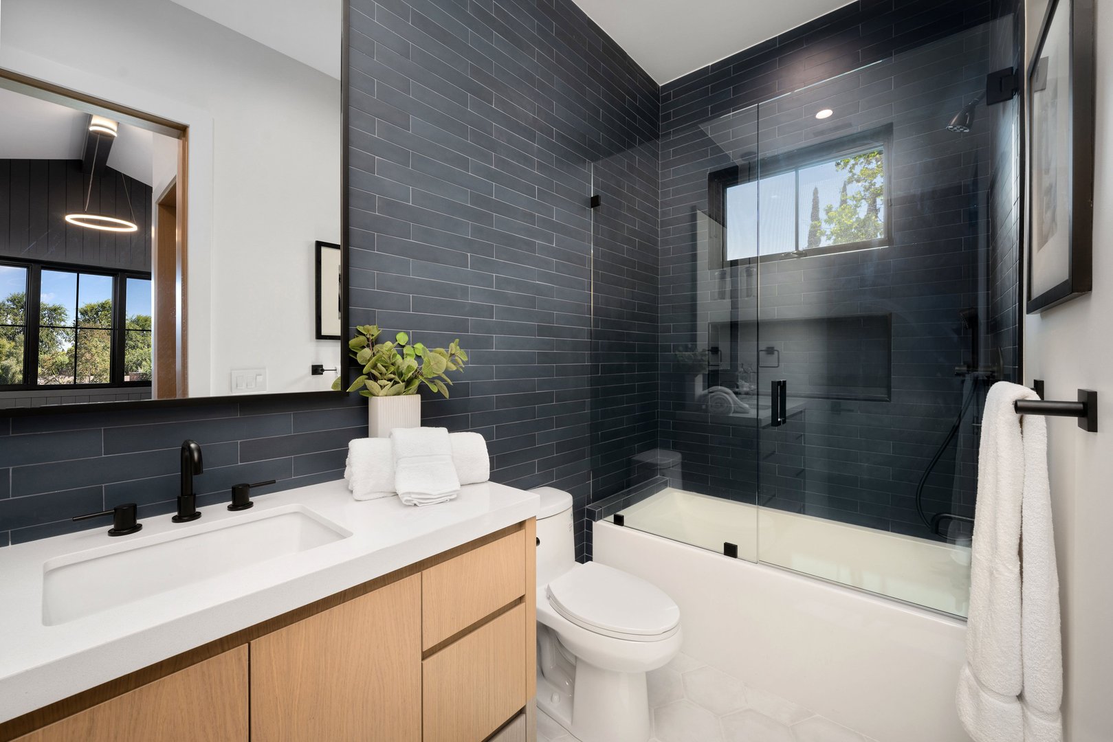 Modern bathroom interior with a sleek design, featuring a glass shower, white vanity, and black tile walls.