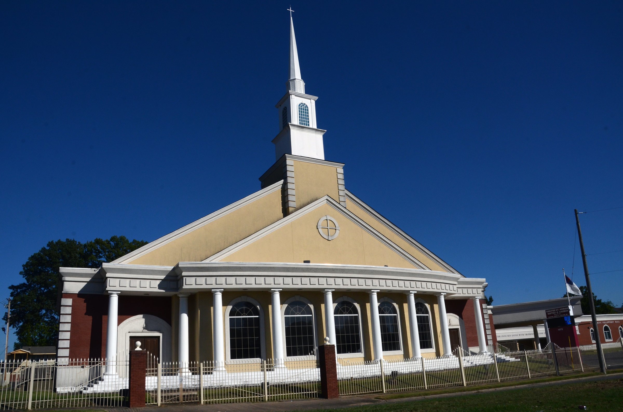 Greater Mount Moriah Baptist Church stands with solemn grace in Memphis, Tennessee, its white steeple and columned facade evoking the enduring legacy of Southern religious architecture. Framed by a clear sky and fenced perimeter, the church reflects both spiritual sanctuary and civic presence. The image captures a moment of architectural reverence, where faith, tradition, and urban rhythm converge. Memphis, TN, USA on September 27, 2025