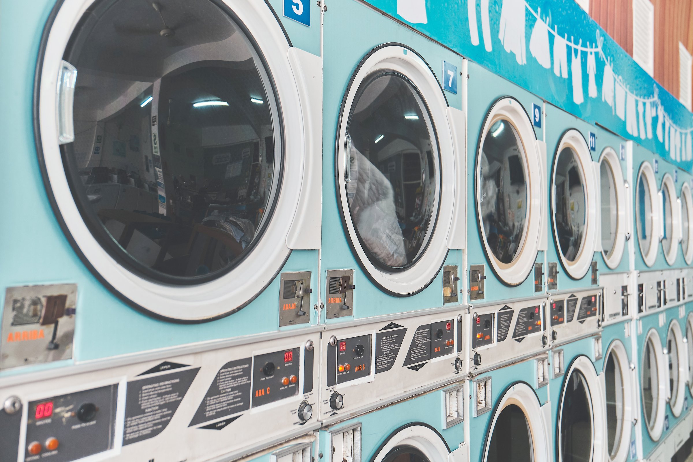 Turquoise industrial dryers are working in a laundromat, drying clothes inside their rotating drums