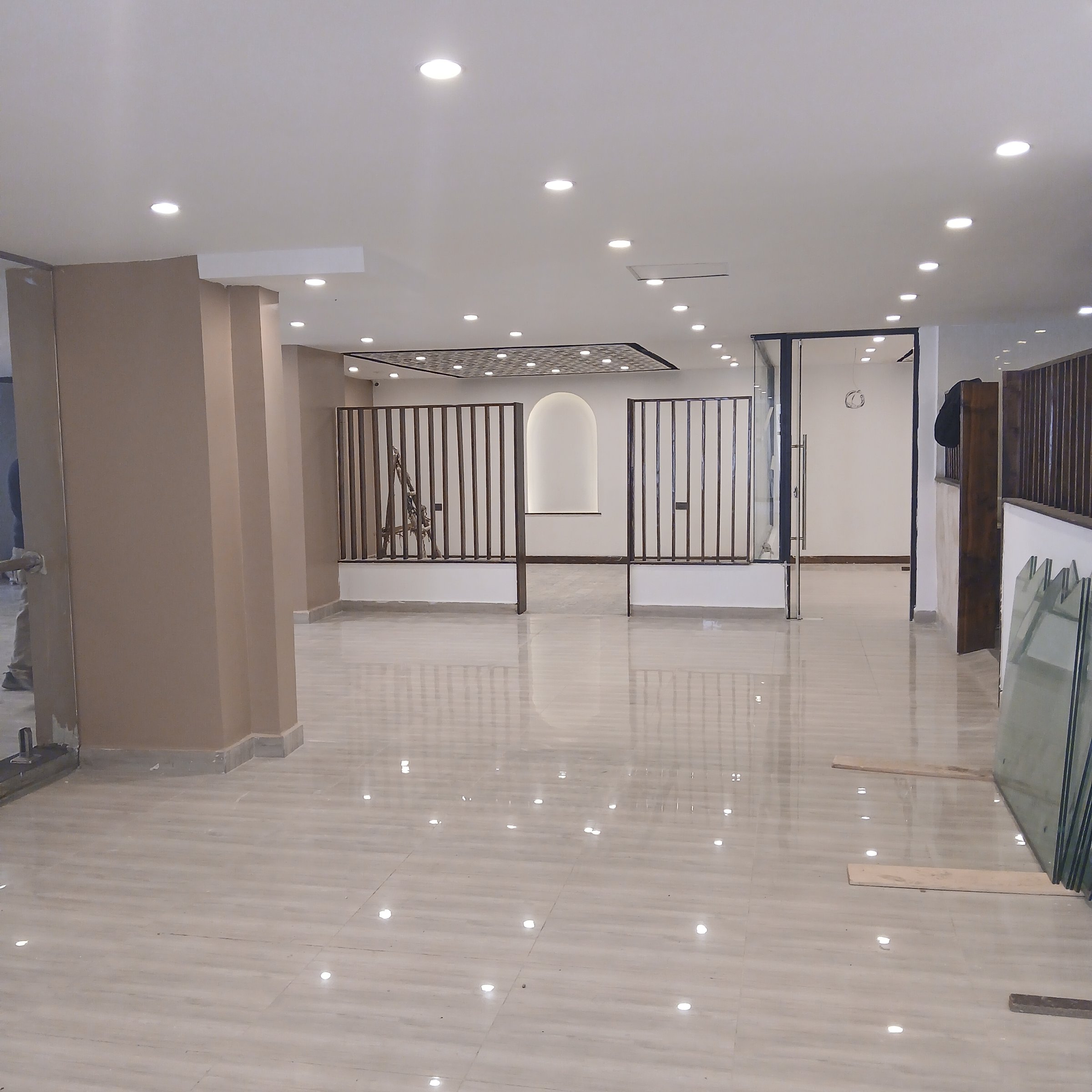 Spacious interior with tiled floor, glass partitions, recessed lighting, and wooden accents, under renovation.