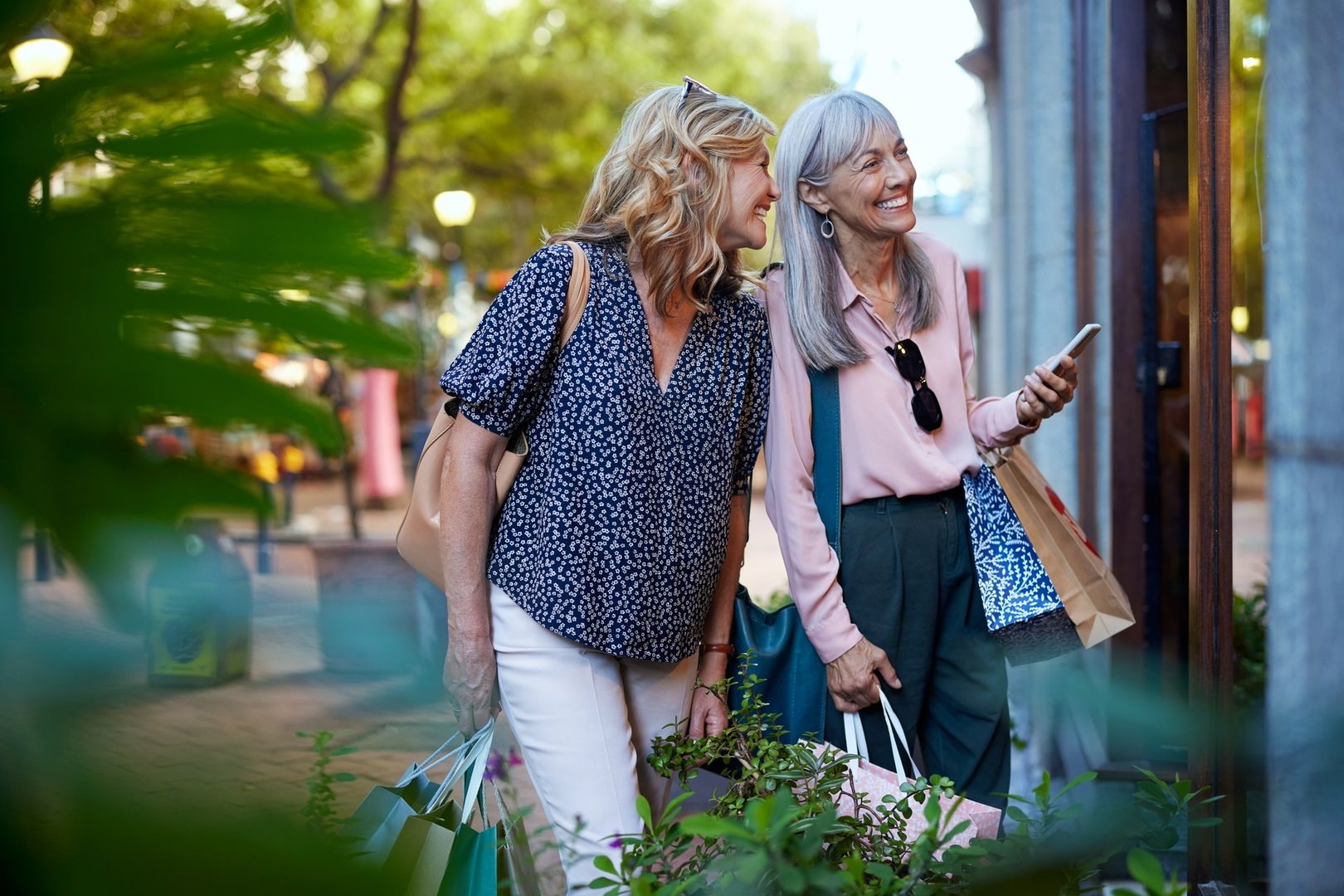 Two older women happily looking at a shop window during shopping time together. Senior ladies enjoying a shopping day during sales. Carefree friends smiling and checking something on display.