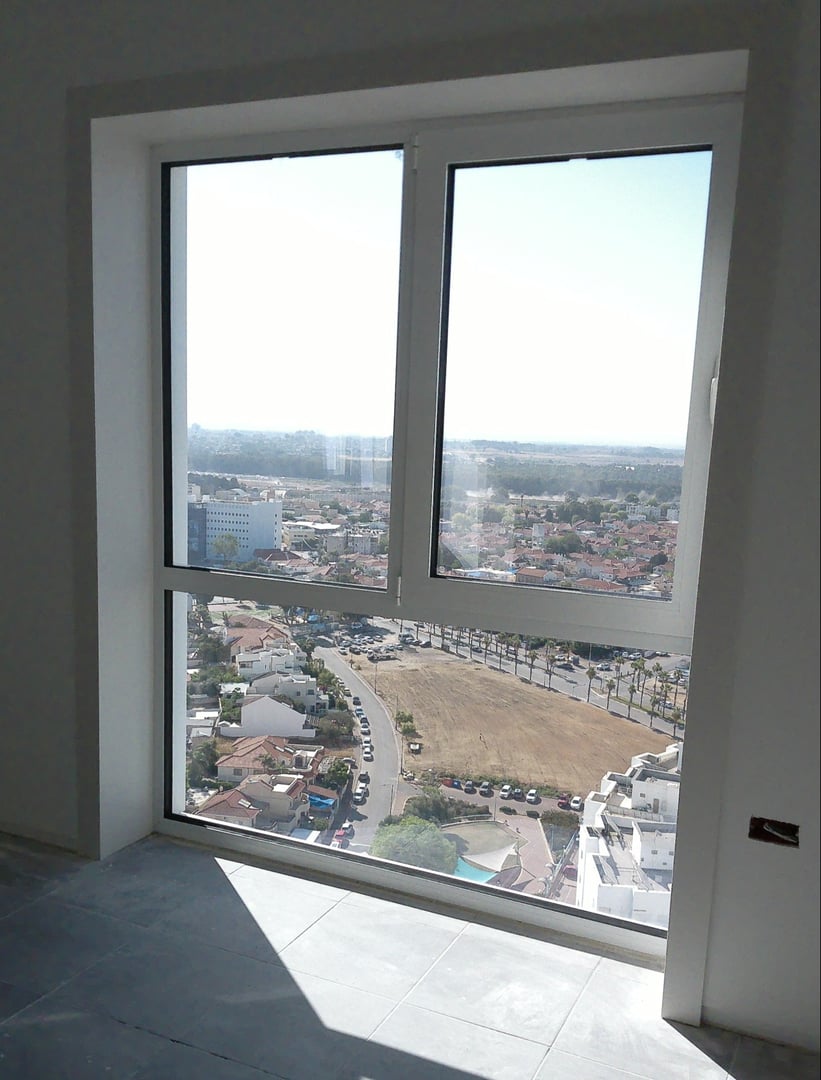 View through a large window in a high-rise building, overlooking a cityscape with buildings, trees, and distant hills.