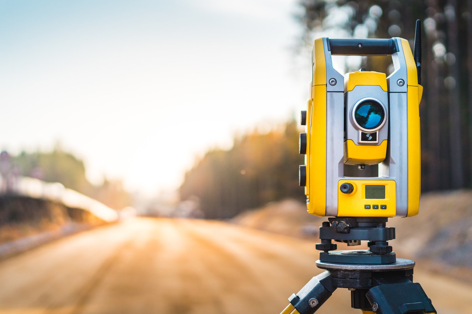 Surveyor engineer with equipment (theodolite or total positioning station) on the construction site of the road or building with construction machinery background