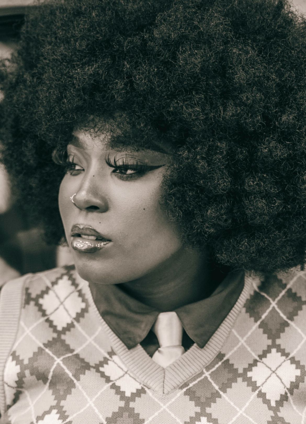 Black and white portrait of a woman with an afro hairstyle, wearing a patterned sweater over a collared shirt.