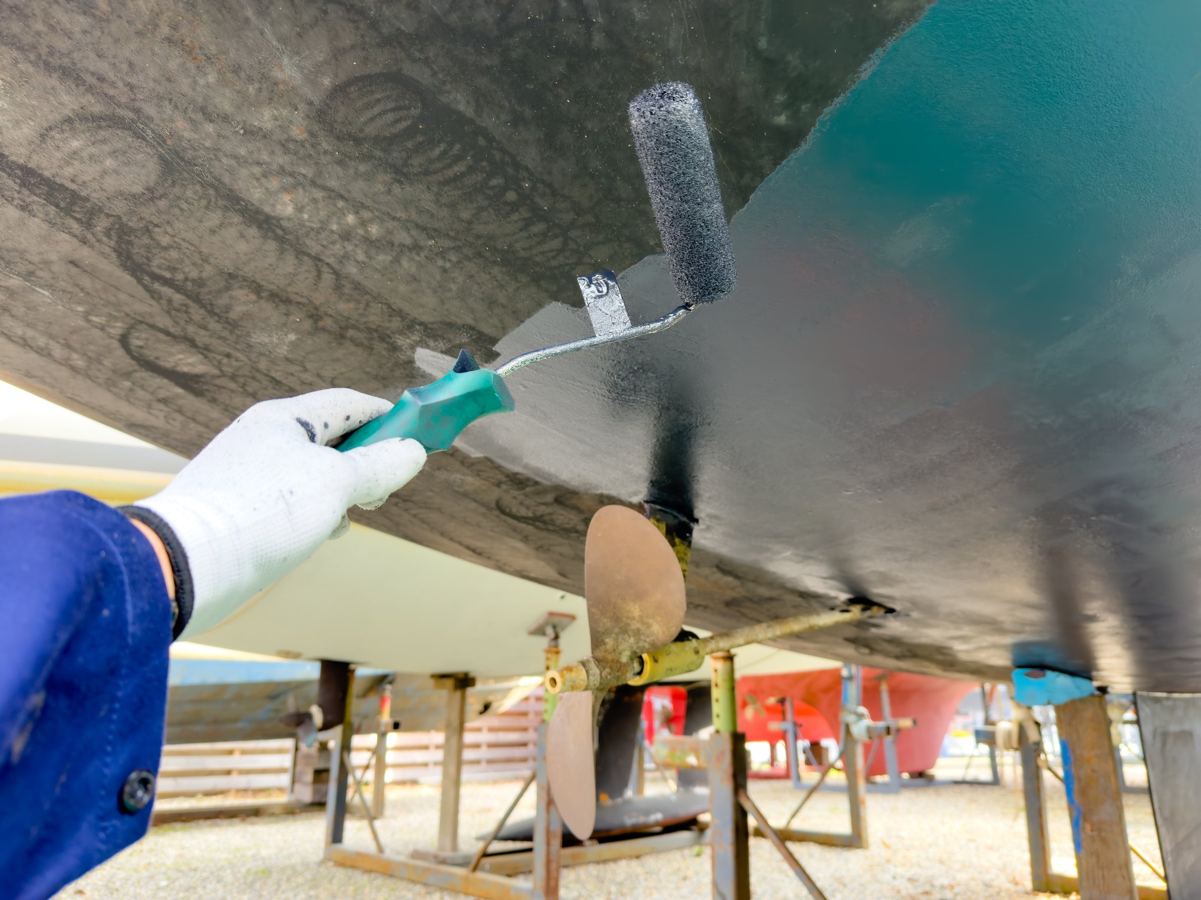 Sailing boat on stilts being painted with antifouling in boatyard