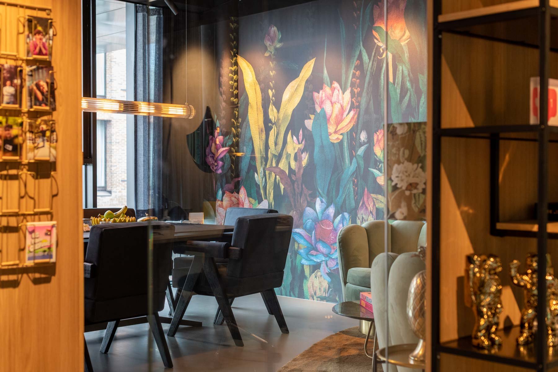 A stylish conference room with a floral mural, dark chairs, modern lighting, and decorative items on shelves.