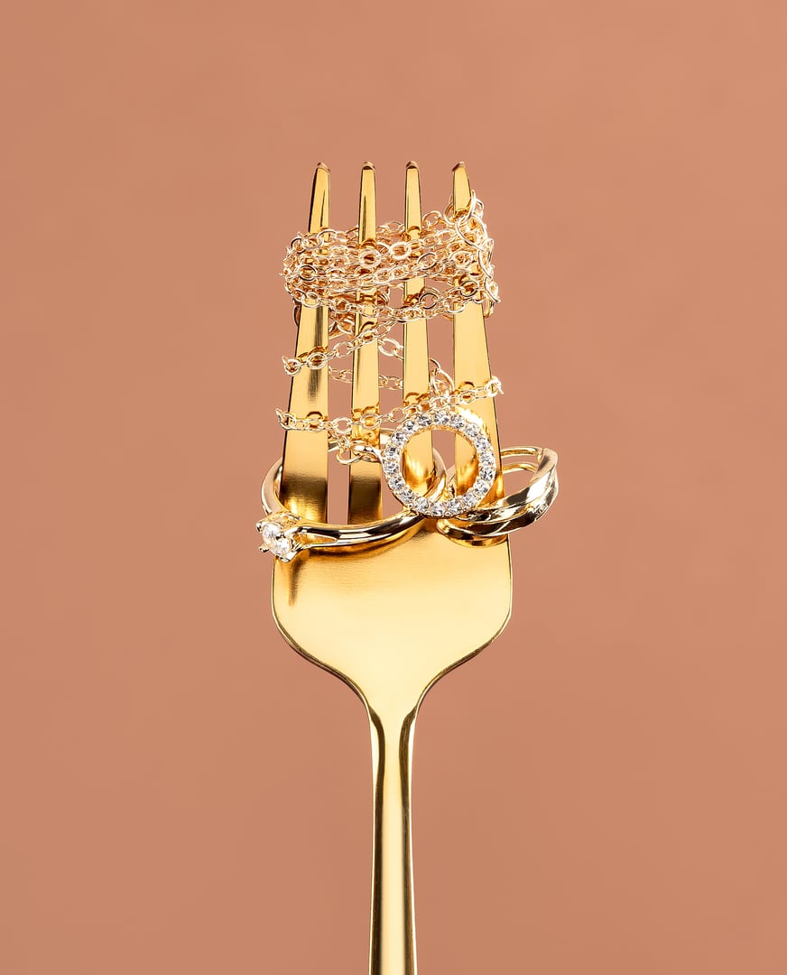 Jewelry background made with golden ring, earrings and necklace put on a fork. Concept of loving gold and jewelry. Studio photography with copy space. Vertical photography.