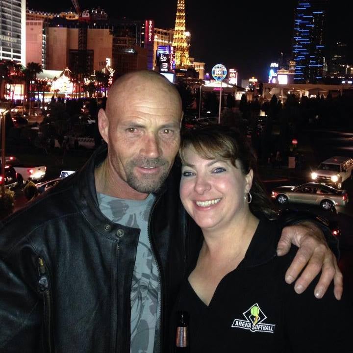 A man and woman smiling together at night with city lights and illuminated buildings in the background.