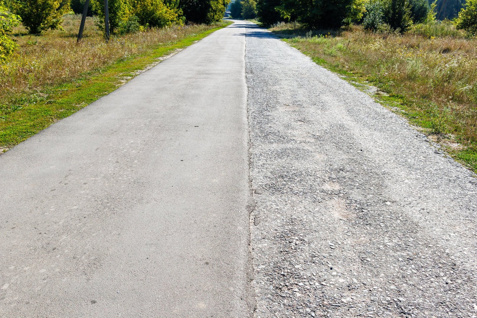 A road of local importance with two lanes of traffic, one half of which is covered with new asphalt to improve the safety of traffic. Half old, half new asphalt road.