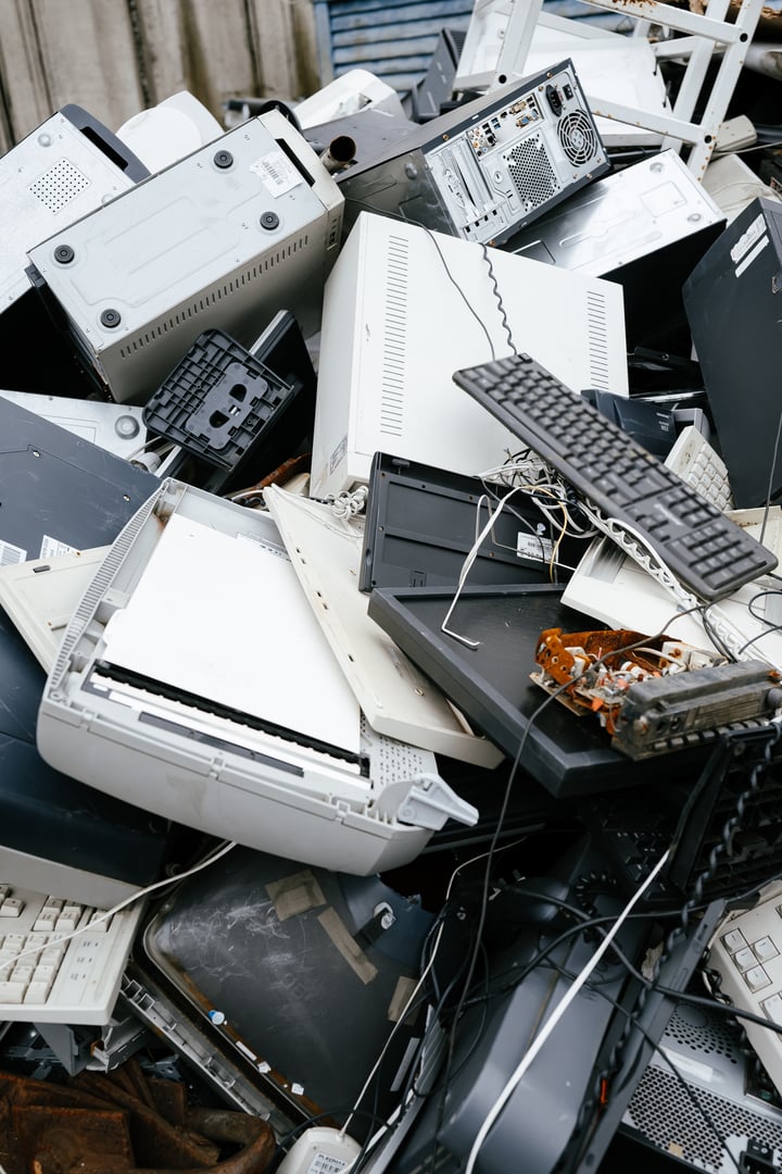 Pile of discarded electronics including computers, monitors, and keyboards highlights e-waste crisis. Stacked electronic debris underscores environmental impact and recycling challenges.
