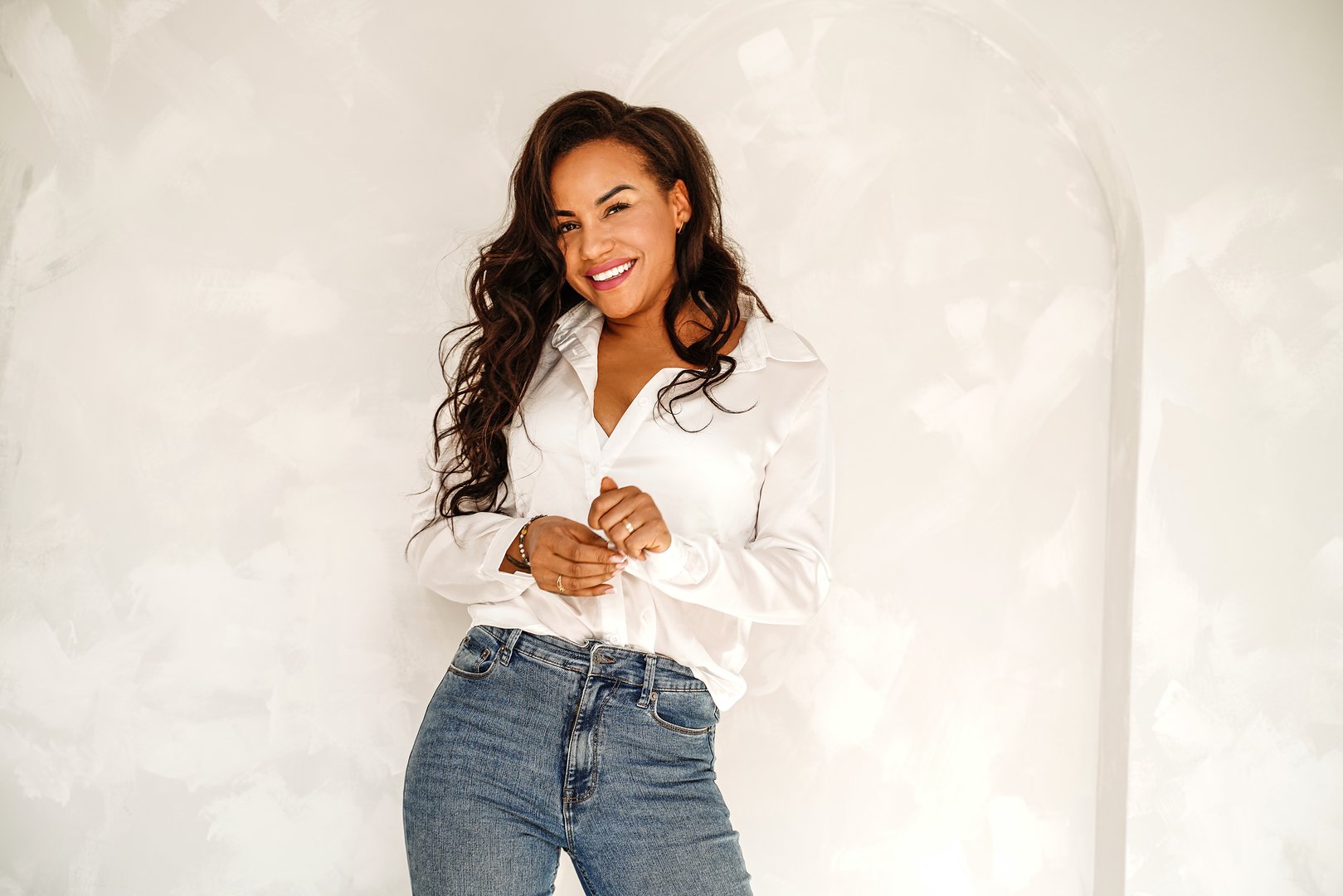 Beautiful woman posing in white shirt and jeans, casual elegant look. Smiling attractive lady with long dark hair looking at the camera. A lot of copy space.