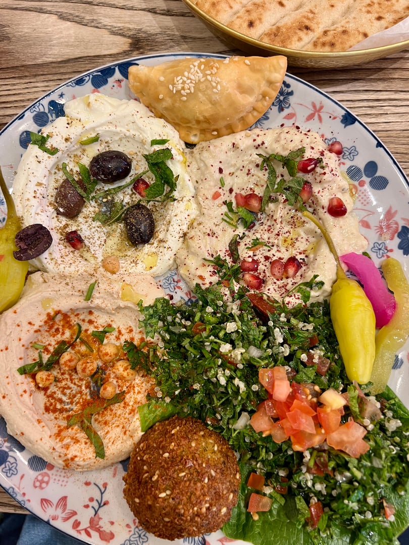 Close up view of a Meze platter with Hummus, Baba Ghanoush , quinoa tabbouleh, falafel, natural labné, cheese samboussek, flatbread and pickles.