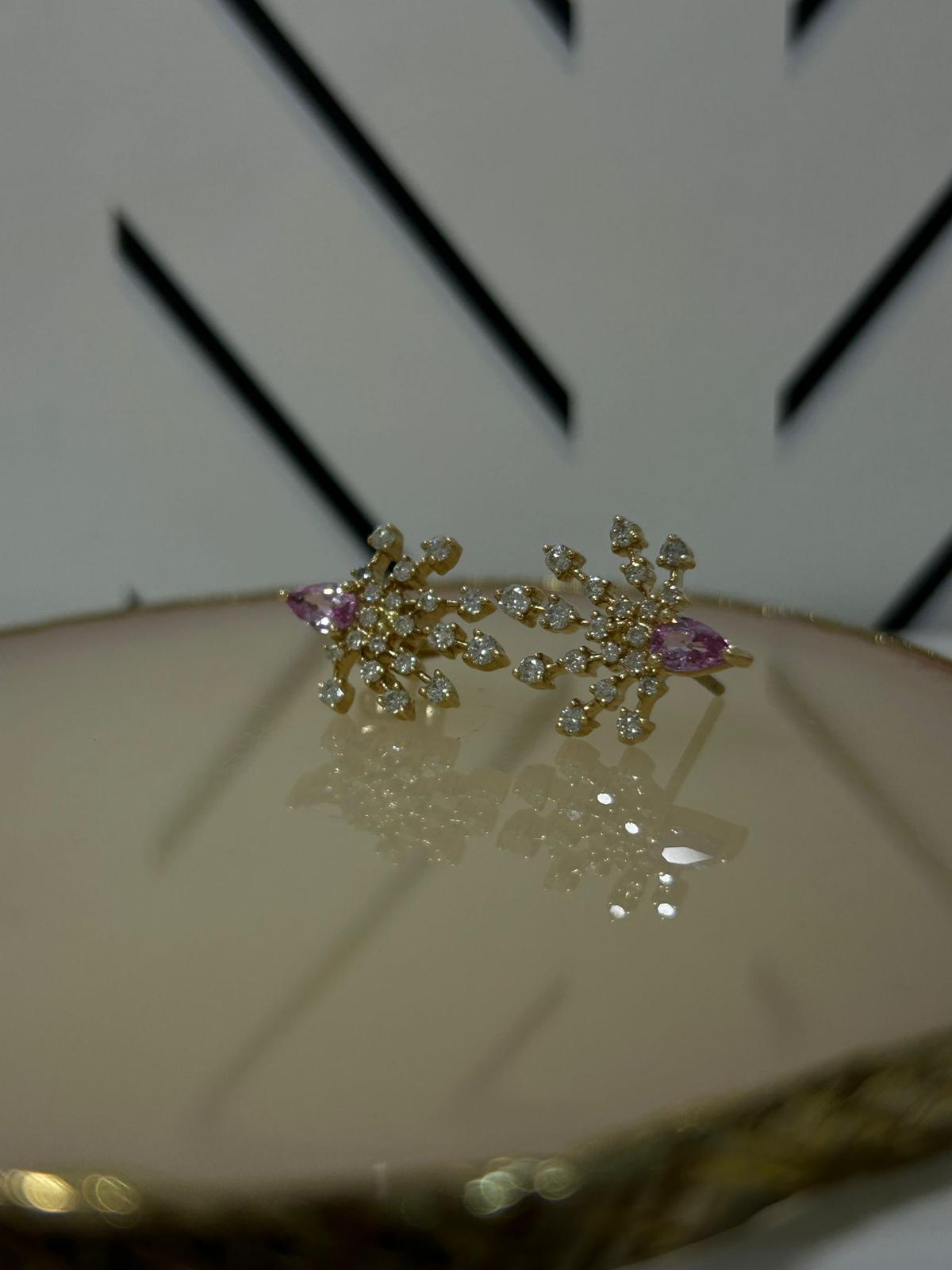 Elegant star-shaped earrings with pink gem accents displayed on a reflective surface against a patterned background.