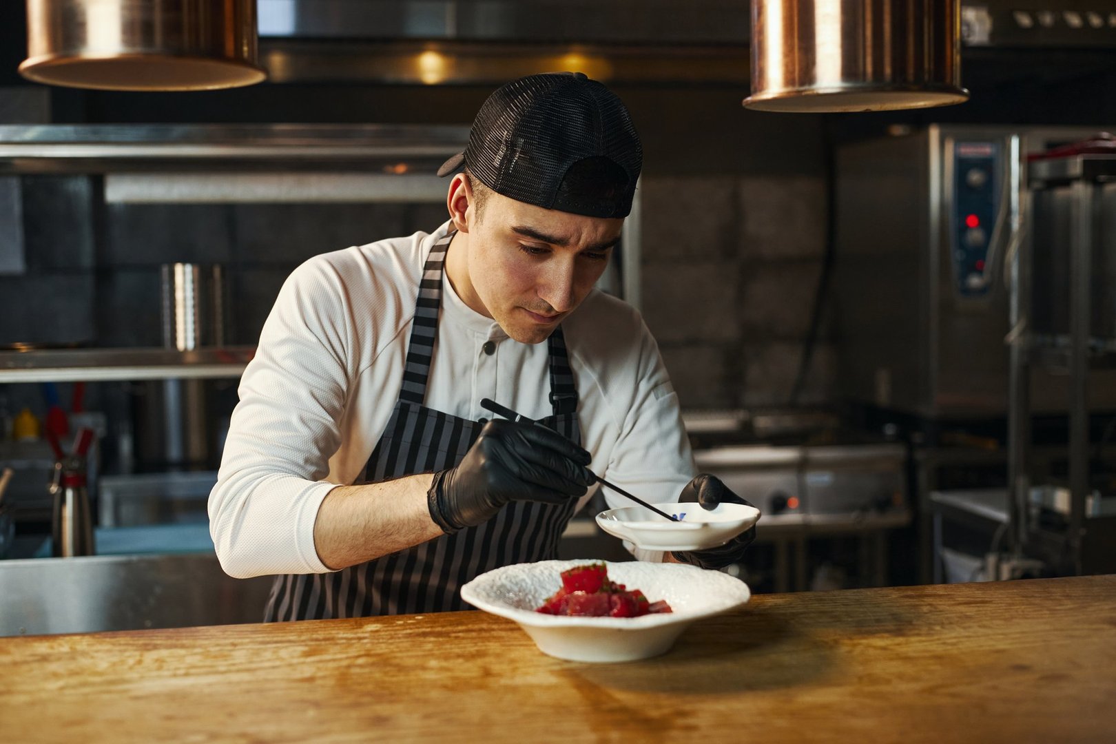 Chef profesional joven preparando platillo gourmet en cocina de restaurante usando guantes de nitrilo para uso gastronómico en México