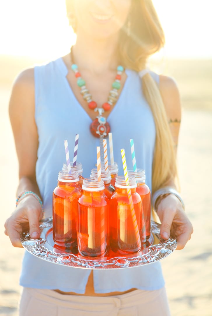 Happy young woman holding a dish with a drinks at sunset beach party