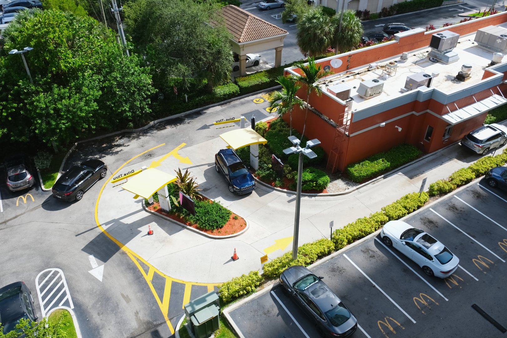 Sunny Isles Beach, FL, USA - June 29, 2022: Aerial view of a McDonald's restaurant building and drive-thru zone with a car at the ordering stand and the parking lot with cars and company logo signs.