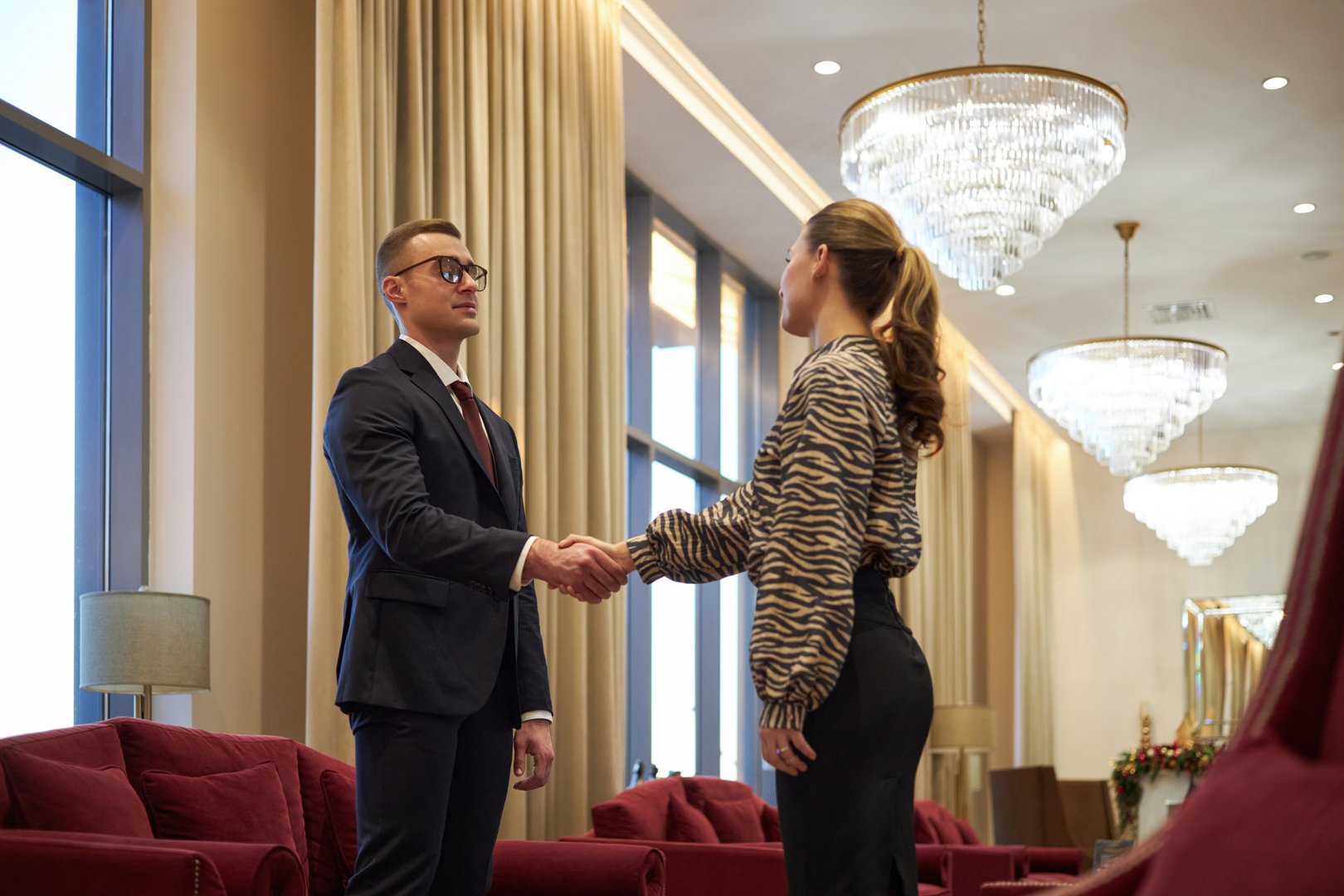 Business professionals shaking hands in modern office under elegant chandeliers and soft lighting