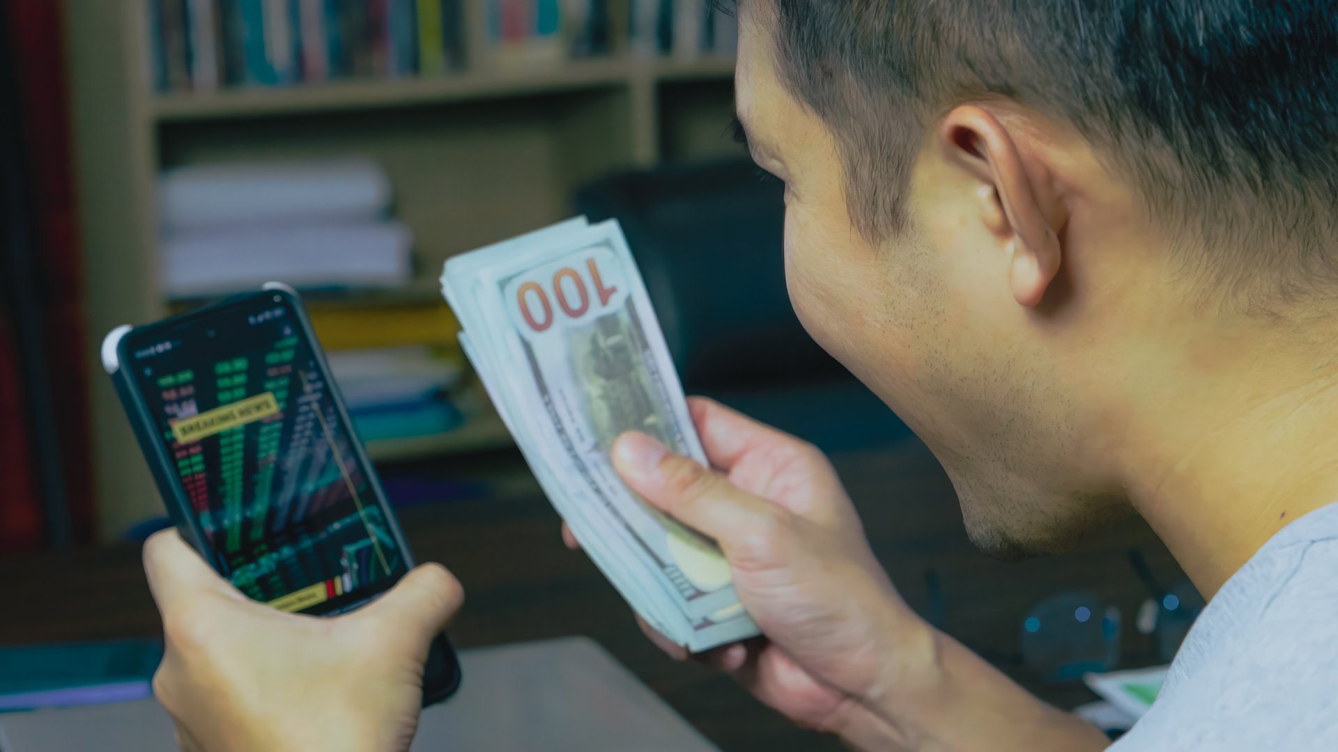 A man counting US Dollars and phone analyzing Crypto Graph at home.