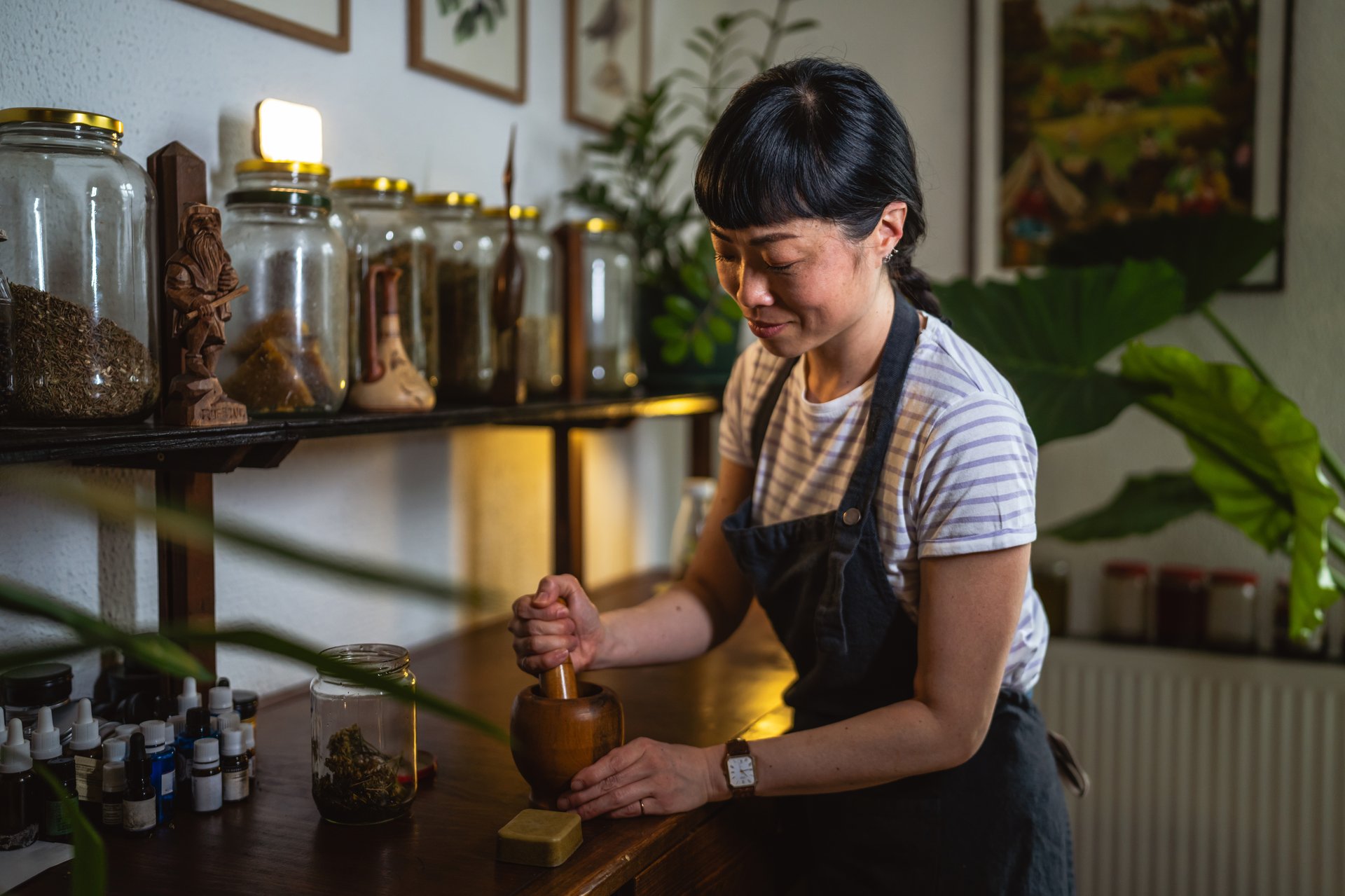 Mature japanese woman wear apron and use mortar and pestle on a wooden table to make soap in herbal workshop