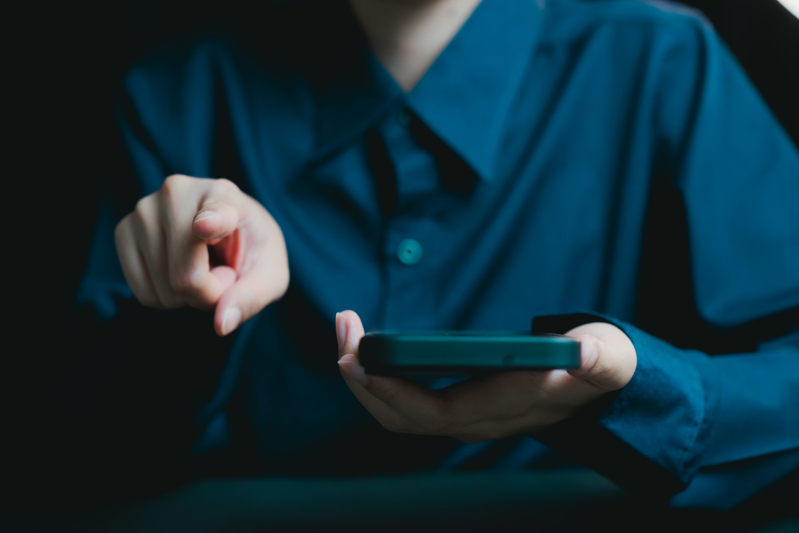 A business professional interacts with a smartphone in a dark environment, demonstrating modern communication and digital engagement. Perfect for business-related themes.