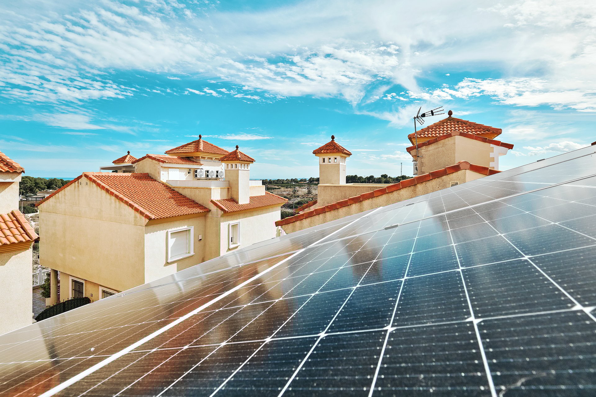 Solar panels installed on red-tiled roofs of residential building on sunny cloudy sky background. Renewable energy sources, eco-friendly housing, modern technology concept