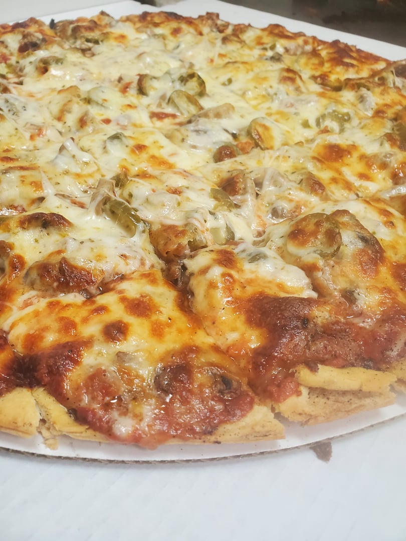 Large pizza with a thick crust, topped with cheese, sausage, and green peppers, on a cardboard surface.