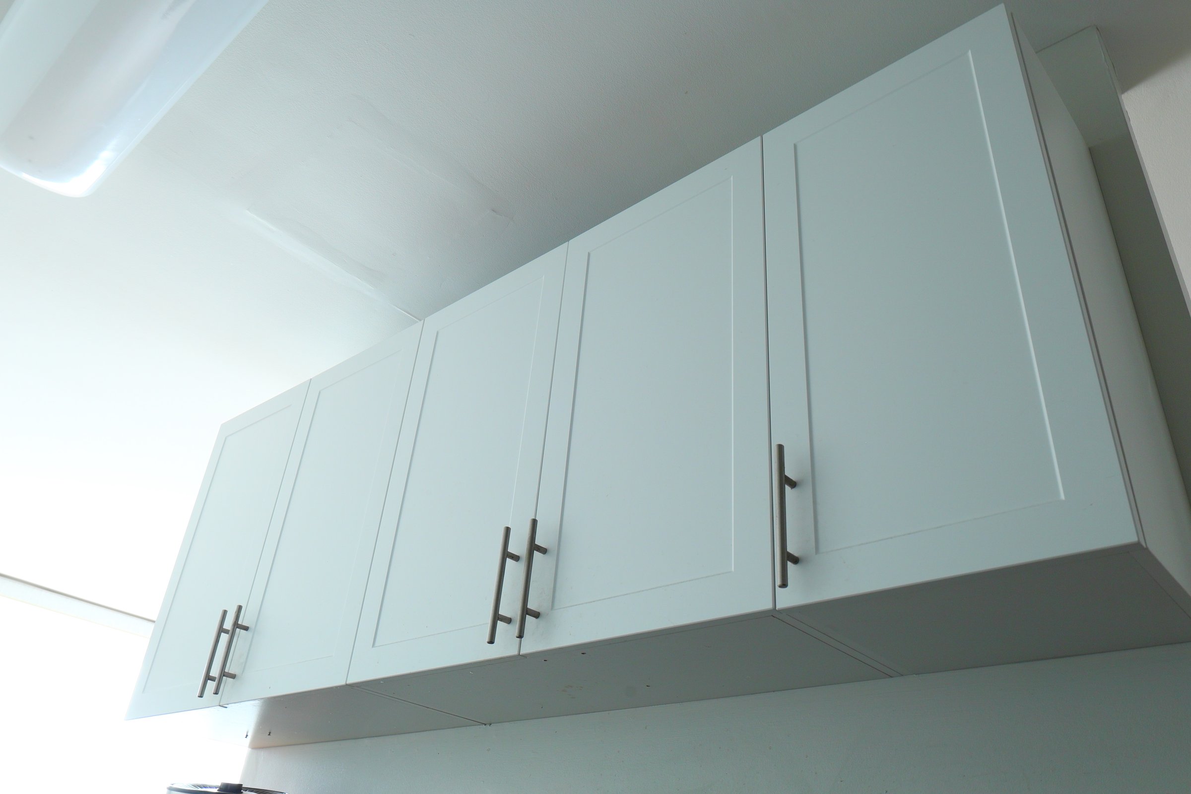 white kitchen cabinets, microwave on top of the fridge, minimalist interior, clean and simple design.