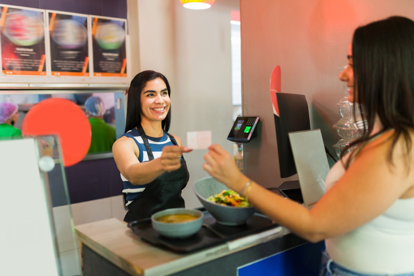 Cheerful cashier receiving loyalty card from customer paying for healthy salad and soup lunch in a fast food restaurant