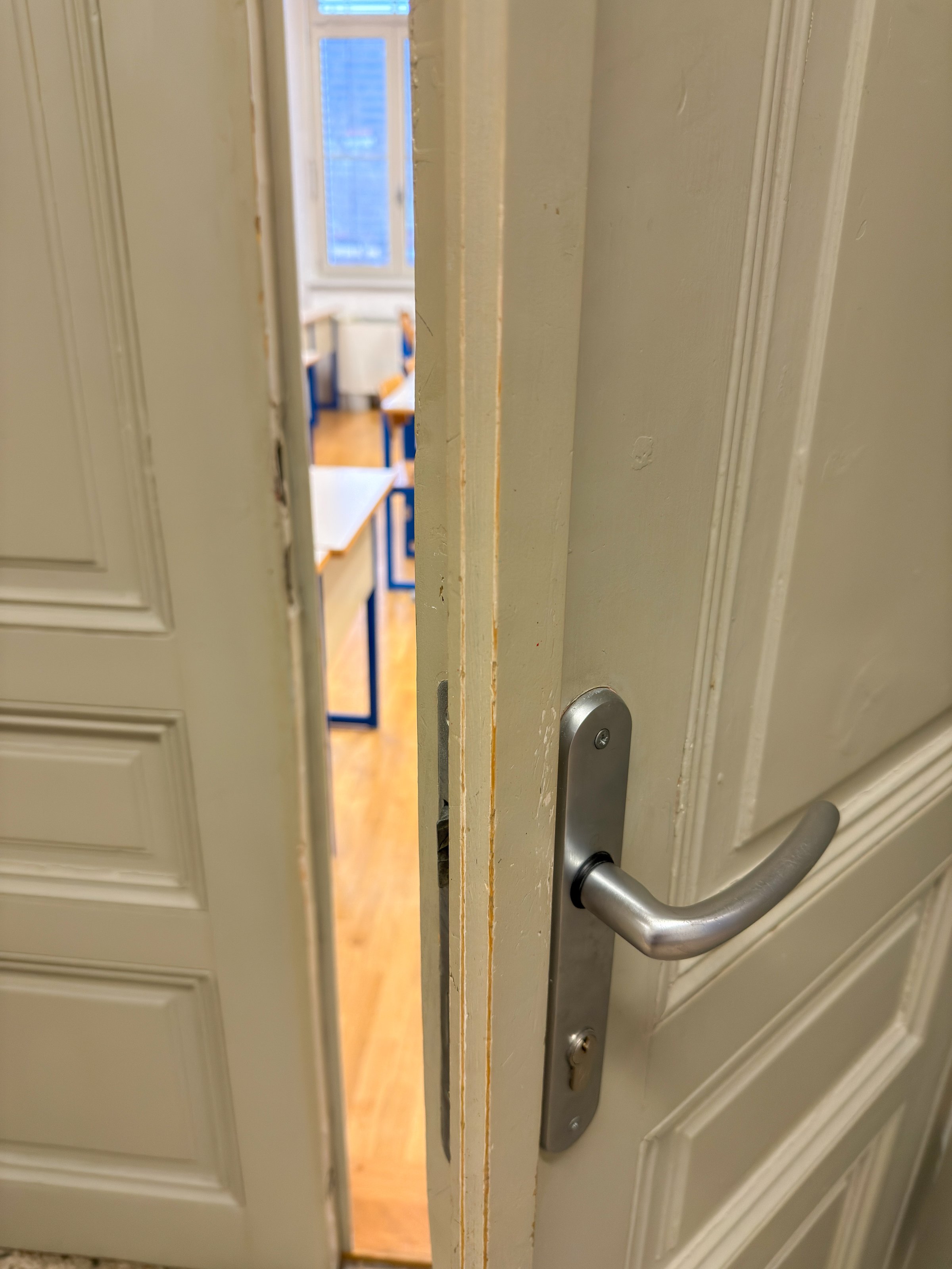 Partially open door leading into a bright classroom with visible desks and chairs.