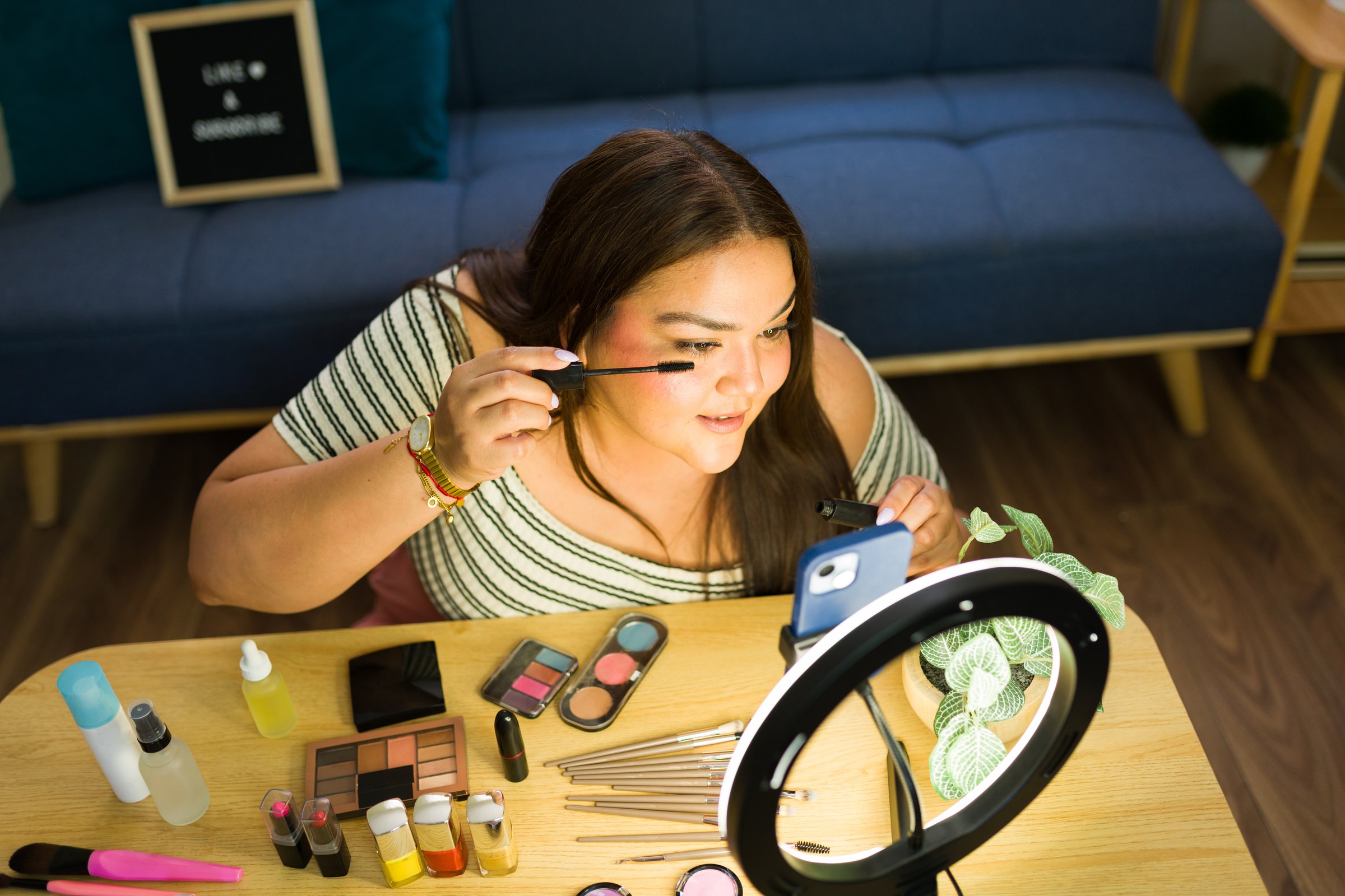 Plus size influencer filming a makeup tutorial for her social media followers using a ring light and a smartphone