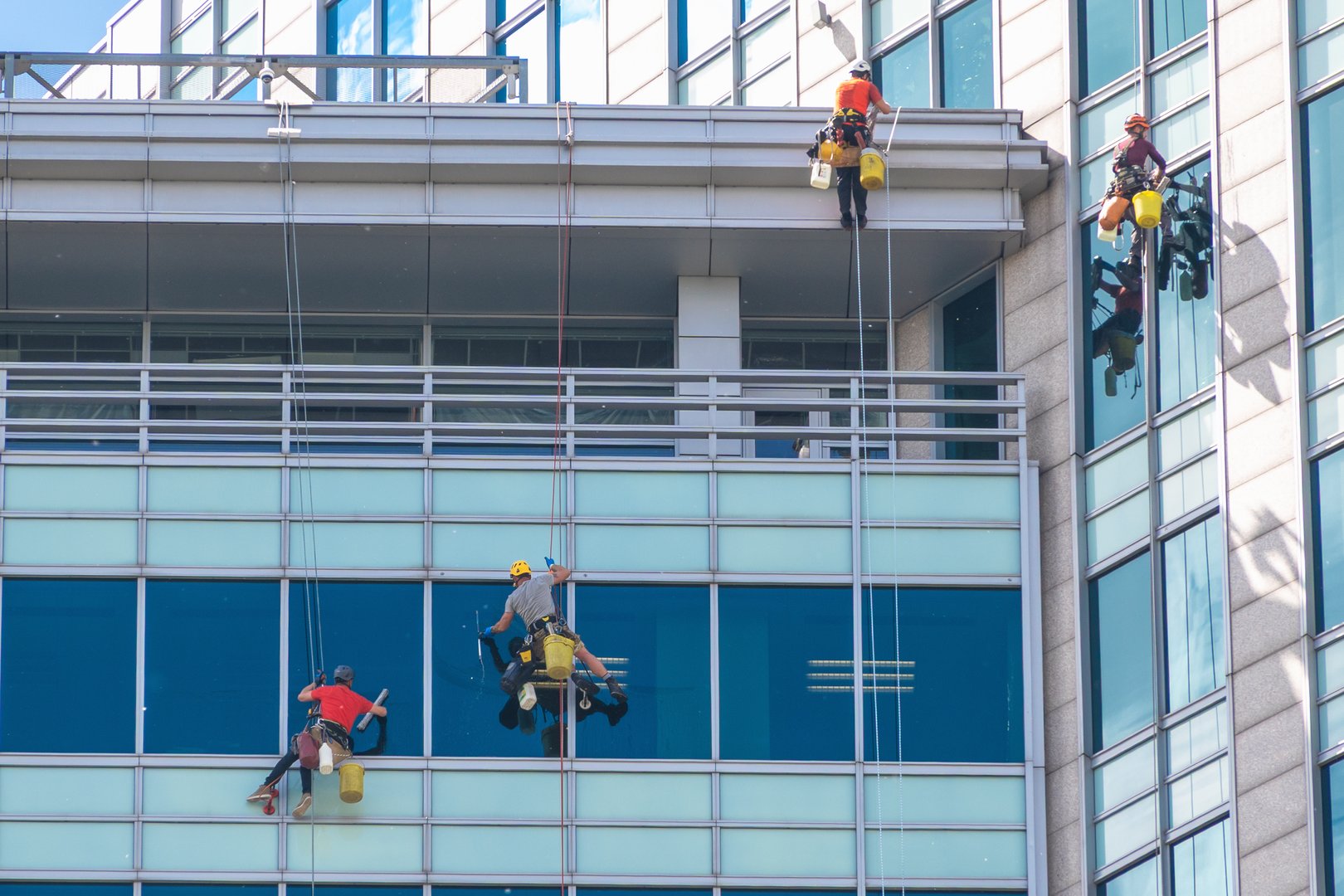 Team of workers cleaning high-rise building windows with ropes. Warsaw, Poland. May 20, 2025