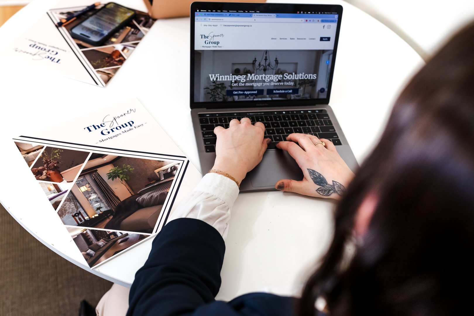 Person using a laptop displaying a mortgage website, with brochures on a table, featuring house interior images.