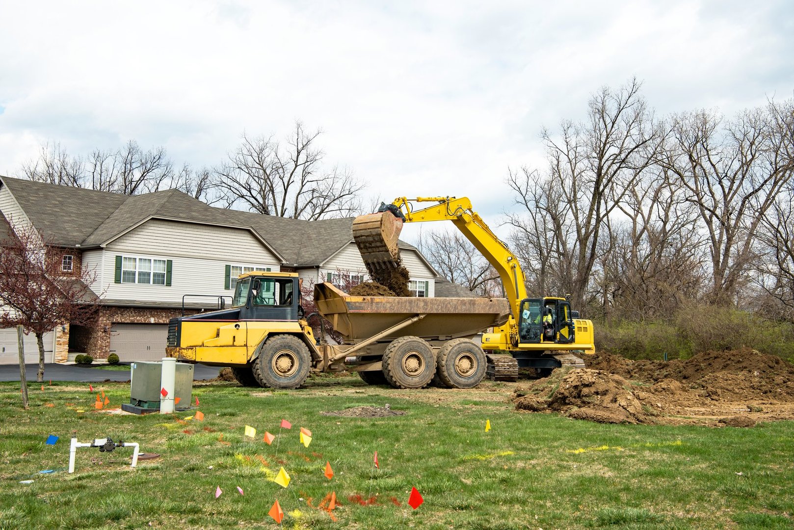 Backhoe loading excavated soil into dump truck bed in preparation for new building construction.