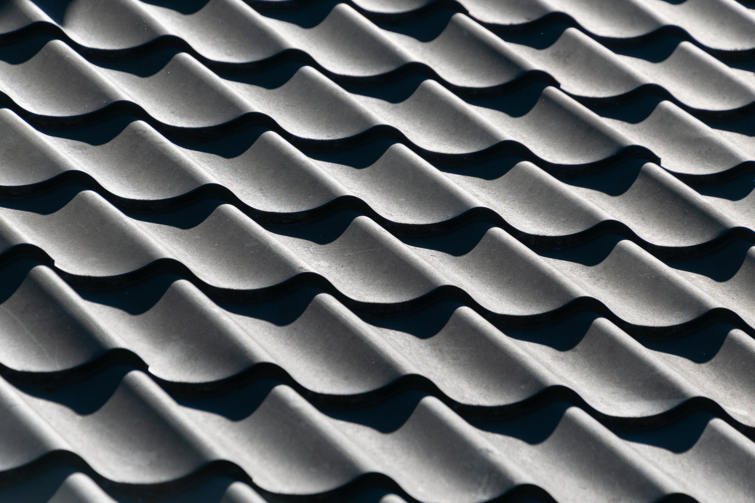 Close-up of textured gray wavy tile roof pattern in sunlight.