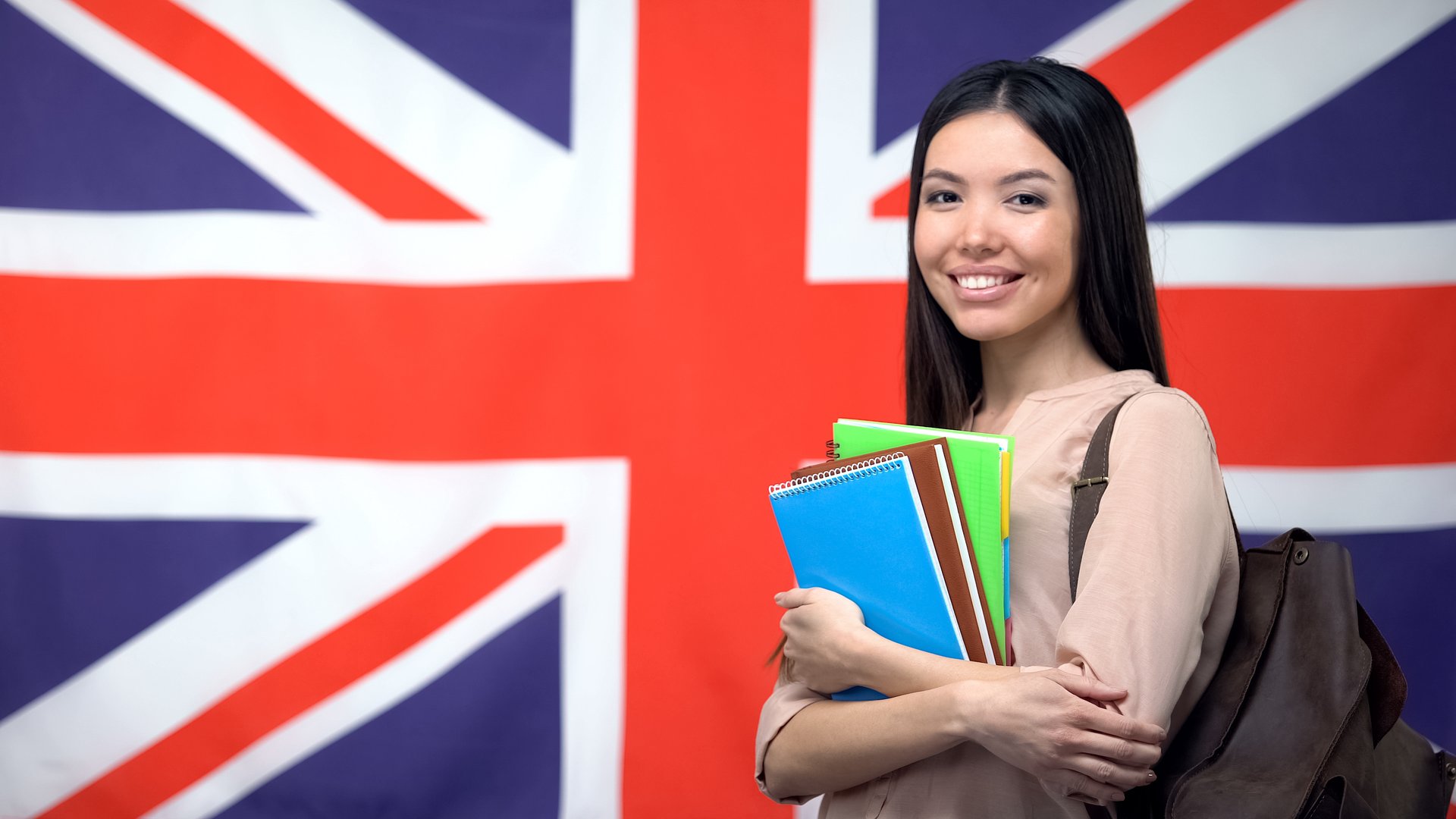 Cheerful Asian woman standing against British flag background, study abroad