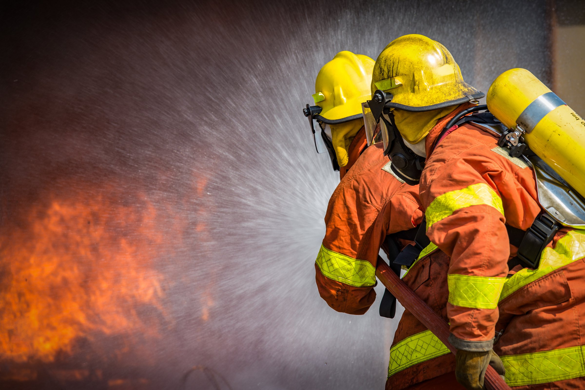 2 firefighters spraying high pressure water to  fire with copy space