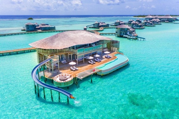 Luxury overwater villa with private pool, water slide, and sun loungers in a clear turquoise sea. Several villas in background.