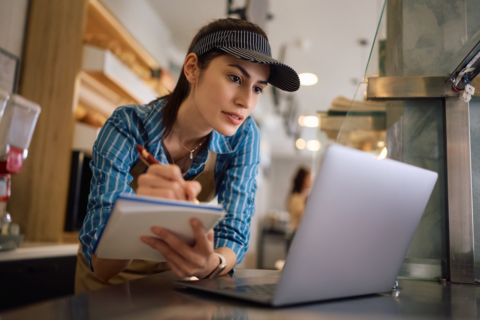 Female worker using laptop and taking notes while working in bakery