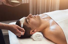 Person lying down with a towel on their forehead while receiving a skincare treatment in a spa setting.